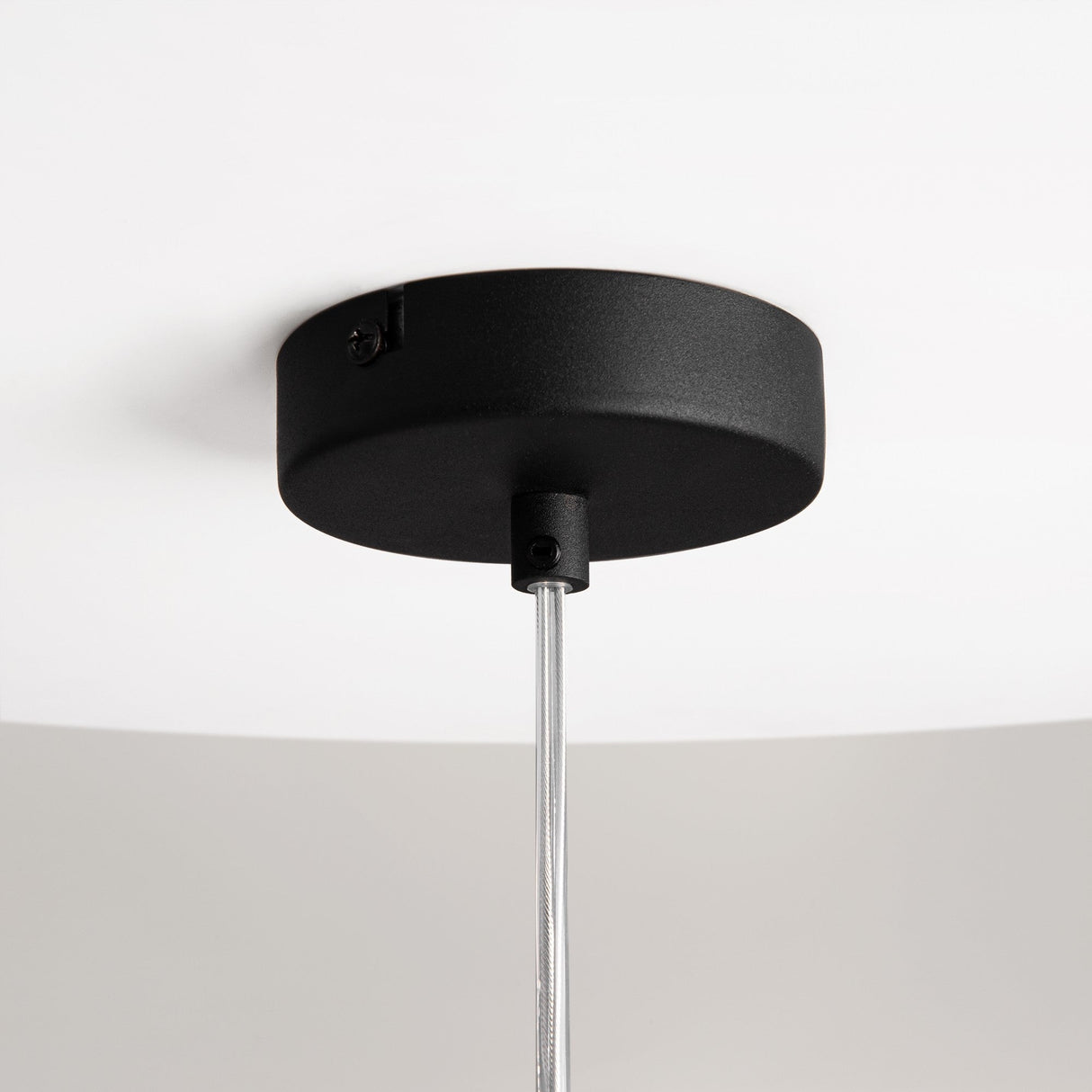 Close-up of the Duality Round Pendant Light, featuring a black circular base and mirrored smoky grey glass shade. A metal rod extends downwards against a white ceiling. The centrally mounted design is modern, minimalistic, and embodies industrial elegance.