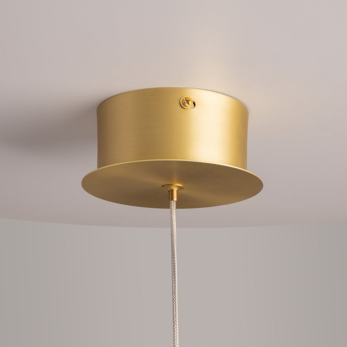 Close-up of the Splash LED Pendant Light 3000K 7W in gold with galvanized grey glass, featuring a satin gold cylindrical fixture and a braided cord. Its elegant design adds modern sophistication against a smooth white ceiling and light gray wall.