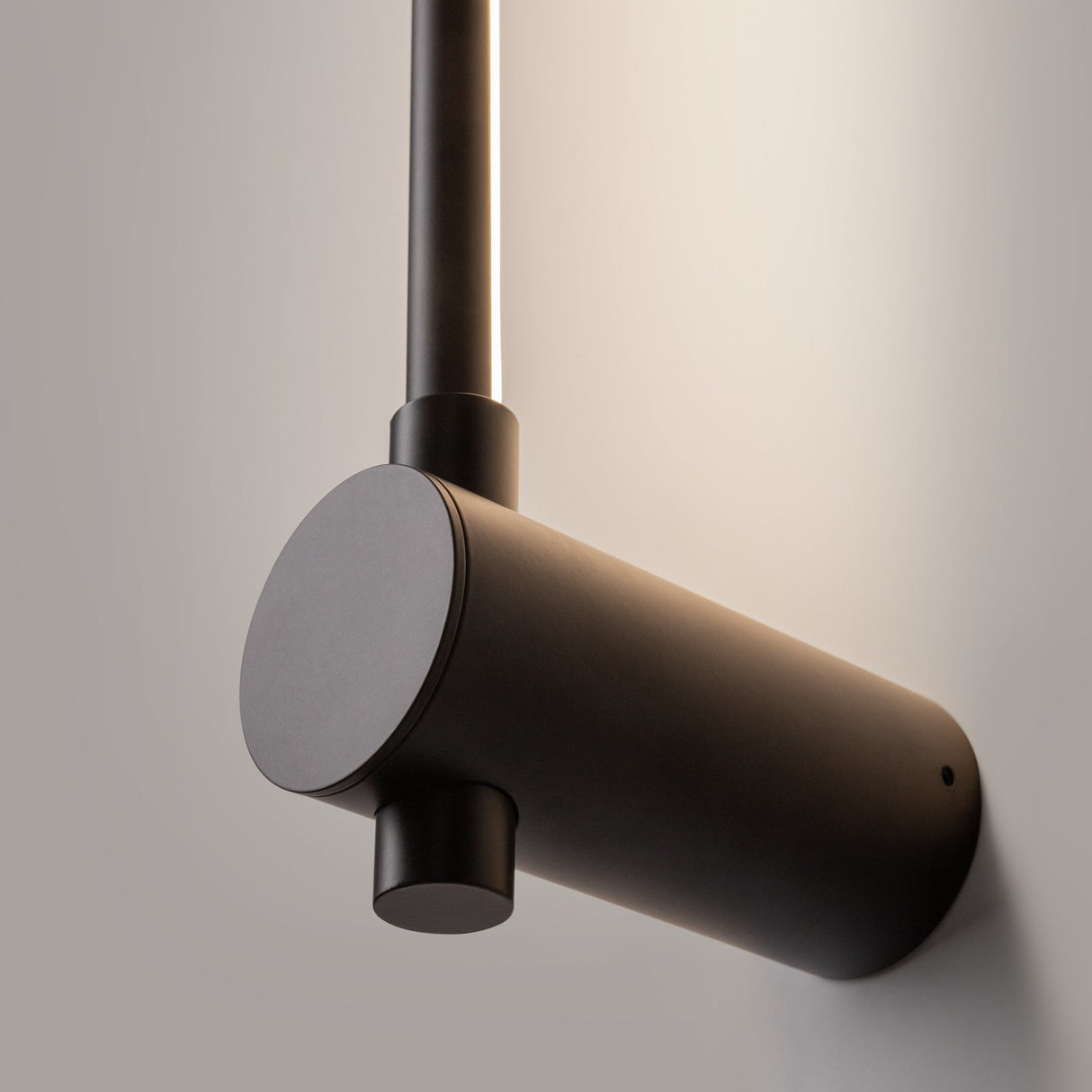 Close-up of the Rotta LED Wall Light 8W 3000K in black featuring a minimalist design with a cylindrical base and vertical rod. It emits soft, adjustable lighting, set against a neutral background.