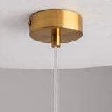 Close-up of the minimalistic and modern Flusso Long Chain Pendant Light - Bronze With Clear Glass Ball, featuring a brass ceiling fixture and round canopy. A clear cord with bronze-finished chains descends against a white ceiling and gray wall.