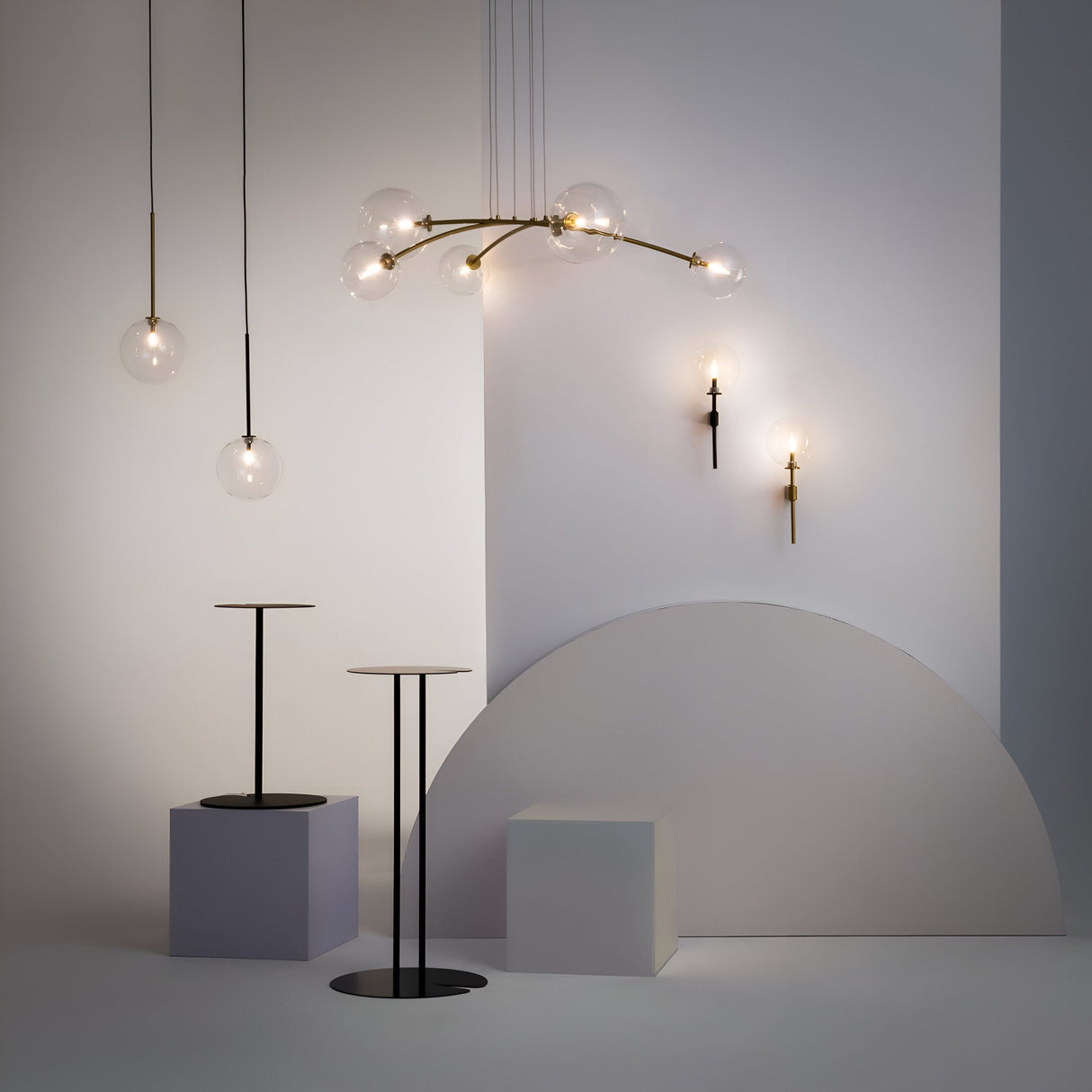 A minimalist interior showcases modern lighting with hanging clear glass globe lights, a geometric tablescape in neutral tones with circles and rectangles, and the Mood Wall Light featuring black metal with clear round glass for an industrial touch.