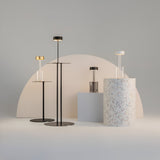 The AI Collaboration Rechargeable LED Table Lamp in black features a sleek design with metallic finishes. It stands on a minimalist backdrop with geometric shapes like a semi-circle and terrazzo-patterned column, providing contemporary style and efficient lighting.