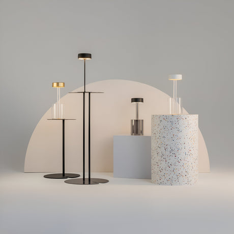 A minimalist display showcases the AI Collaboration Rechargeable LED Table Lamp with a circular base and cylindrical shade set beside a sleek glass vase on a terrazzo pedestal, all against a large semi-circular backdrop, creating a sleek and contemporary setting.