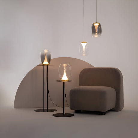 A minimalist room with a beige armchair, arched wall backdrop, and four modern lamps. Two Splash LED Table Lamps on black stands and two gold hanging lamps with clear glass shades create a warm atmosphere.