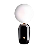 The Pallo Table Lamp - Black features a glossy black cylindrical base and a large round opal glass diffuser, displayed against a plain white background.