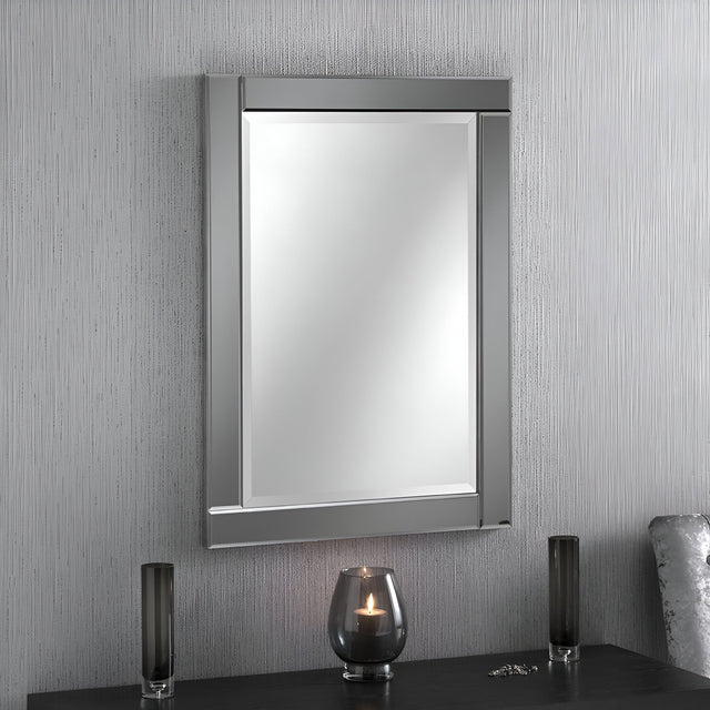 The Lustro Rectangle Wall Mirror in grey, measuring 89x64cm, is mounted on a vertically striped textured wall. Below it, a black tabletop displays a lit candle in a glass holder, accompanied by two sleek black vases, creating a modern aesthetic.