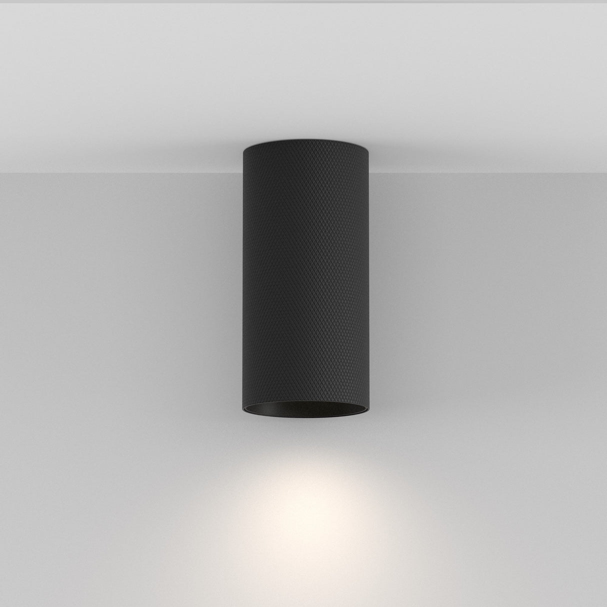 The Artisan Single Fixed Round Surface Mounted Downlight in black is a modern lighting solution with a cylindrical design for white ceilings. It casts a soft circular glow downward and has a textured finish, offering minimalist and sleek appeal.