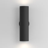 The Artisan Wall Light - Black is a cylindrical, wall-mounted fixture made of black aluminum that provides ambient lighting with a soft white glow above and below on a plain gray wall.