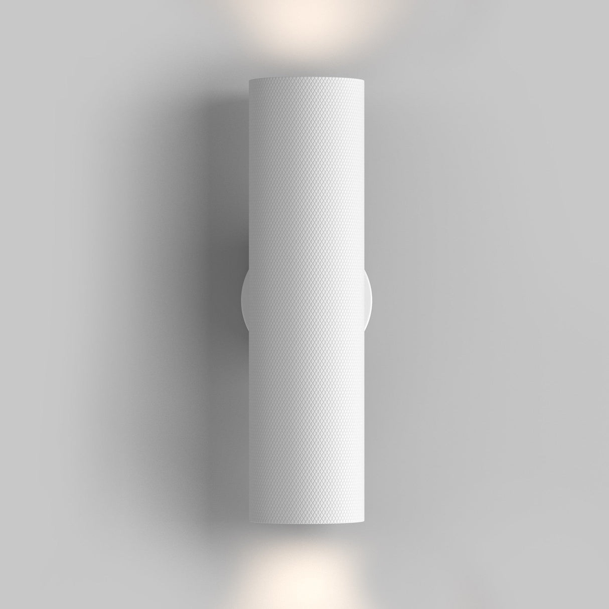 The Artisan Wall Light - White is a modern, white cylindrical fixture with a textured aluminum body. Mounted vertically on a light gray background, it emits soft light from the top and bottom, embodying minimalism and creating a gentle wall glow.