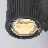 Close-up of the sleek, corrosion-resistant Rando Outdoor Up & Down Wall Light in grey, adorned with water droplets. The illuminated fixture casts a warm glow, emphasizing the textured ridges on its dark cylindrical design.