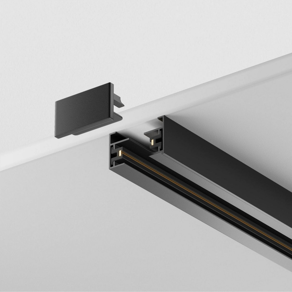 Close-up of a Unity Single Phase Surface-Mounted Track 2m in black, L-shaped and mounted on a white ceiling. A detached end cap near the rail’s open end shows inner components and wiring channels, ideal for customized lighting setups.