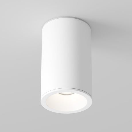 A modern, cylindrical Zoom Small Round Surface Downlight in white is mounted on a light gray ceiling. It emits a soft, warm glow from its round opening, providing a minimalist look with an IP65 rating for enhanced durability.