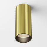 A Focus LED Fixed Round Surface Mounted Downlight 12W 3000K in brass with a sleek, modern cylindrical design hangs from a white ceiling, featuring an energy-efficient recessed bulb and smooth metallic appearance.