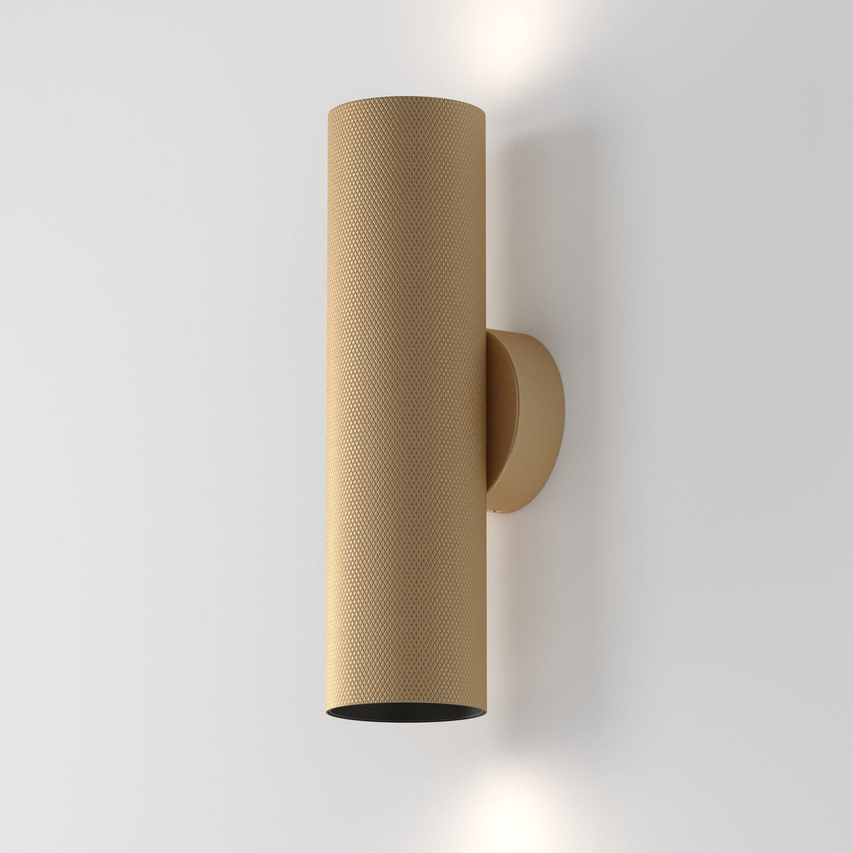 The Artisan Wall Light - Matte Gold is a contemporary design masterpiece with a modern cylindrical shape and perforated texture. Mounted vertically on a white wall, it casts soft light both upward and downward gracefully.