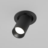 The Artisan Single Tilt Round Recessed Downlight - Black features a sleek cylindrical design with a ribbed texture and focused beam, reflecting modern industrial style, perfectly complementing a light gray background.