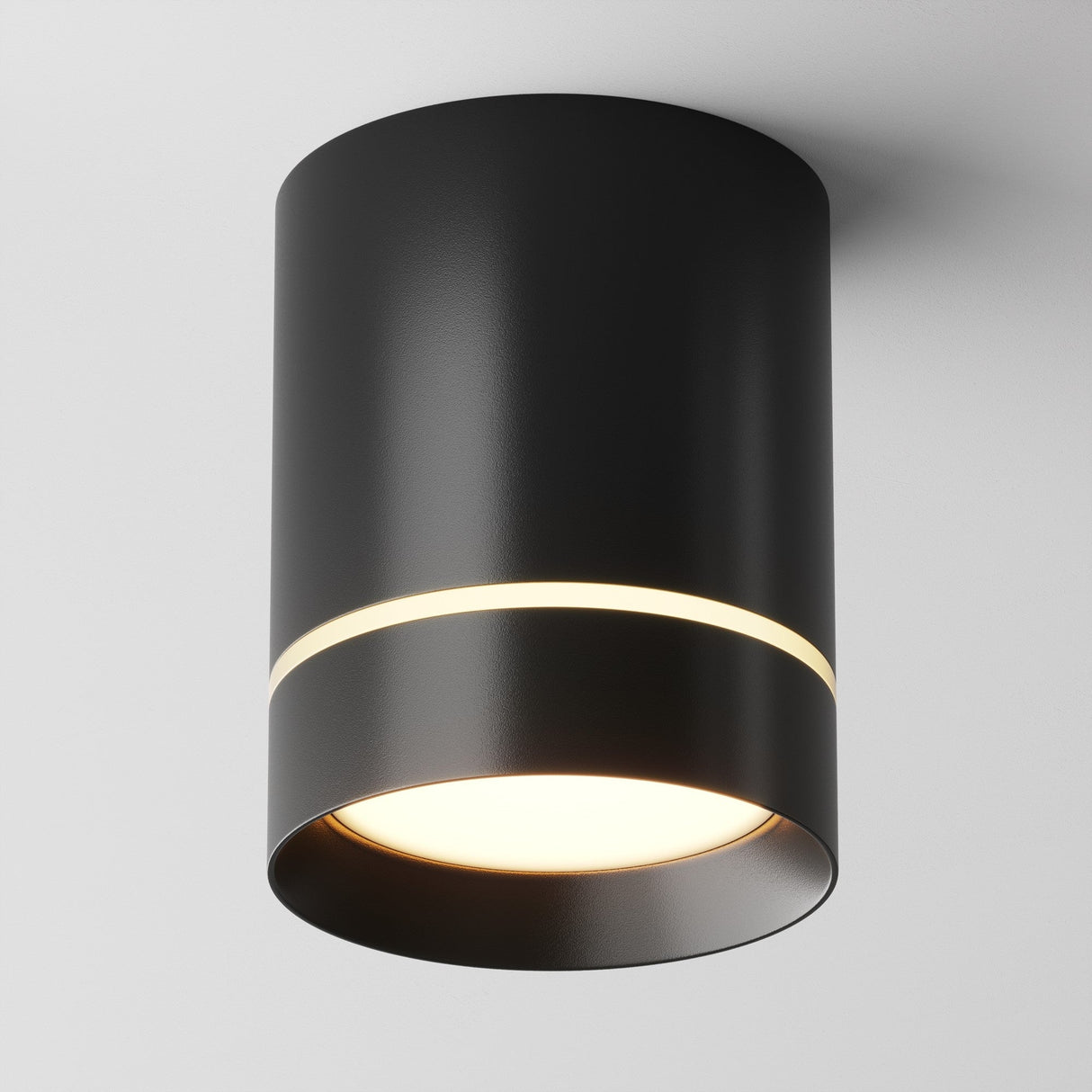 The Orlo LED Round Surface Downlight 9W 3000K - Black features a modern cylindrical design with a matte black finish that emits white light from the bottom and has a thin circumferential gap, adding sleekness to its energy-efficient design against any plain white ceiling.