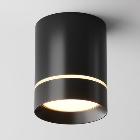 The Orlo LED Round Surface Downlight 9W 3000K - Black features a modern cylindrical design with a matte black finish that emits white light from the bottom and has a thin circumferential gap, adding sleekness to its energy-efficient design against any plain white ceiling.