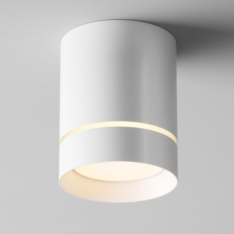 The Orlo LED Round Surface Downlight 9W 3000K in white is a modern ceiling fixture with a minimalist cylindrical design, features a narrow top gap for a soft glow, and complements its main downward light. Its energy-efficient and mounts seamlessly onto a white ceiling.