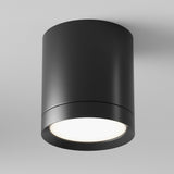 The Hoop Medium Round Surface Downlight - Black is a sleek, cylindrical LED fixture that emits a soft, bright light against a plain white background. Perfect for modern interiors, this stylish downlight enhances any room with its elegant simplicity and energy-efficient design.