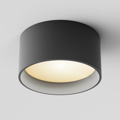 The Vega LED Round Surface Downlight 15W 3000K - Black, with its modern cylindrical design and matte black finish, emits warm yellow light from a white ceiling, illuminating the space softly.