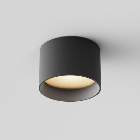 The Vega LED Round Surface Downlight 8W 3000K - Black, a modern cylindrical fixture, shines warmly against a white ceiling. Its energy-efficient lighting casts subtle shadows, emphasizing its sleek, minimalist design and sophisticated black finish.