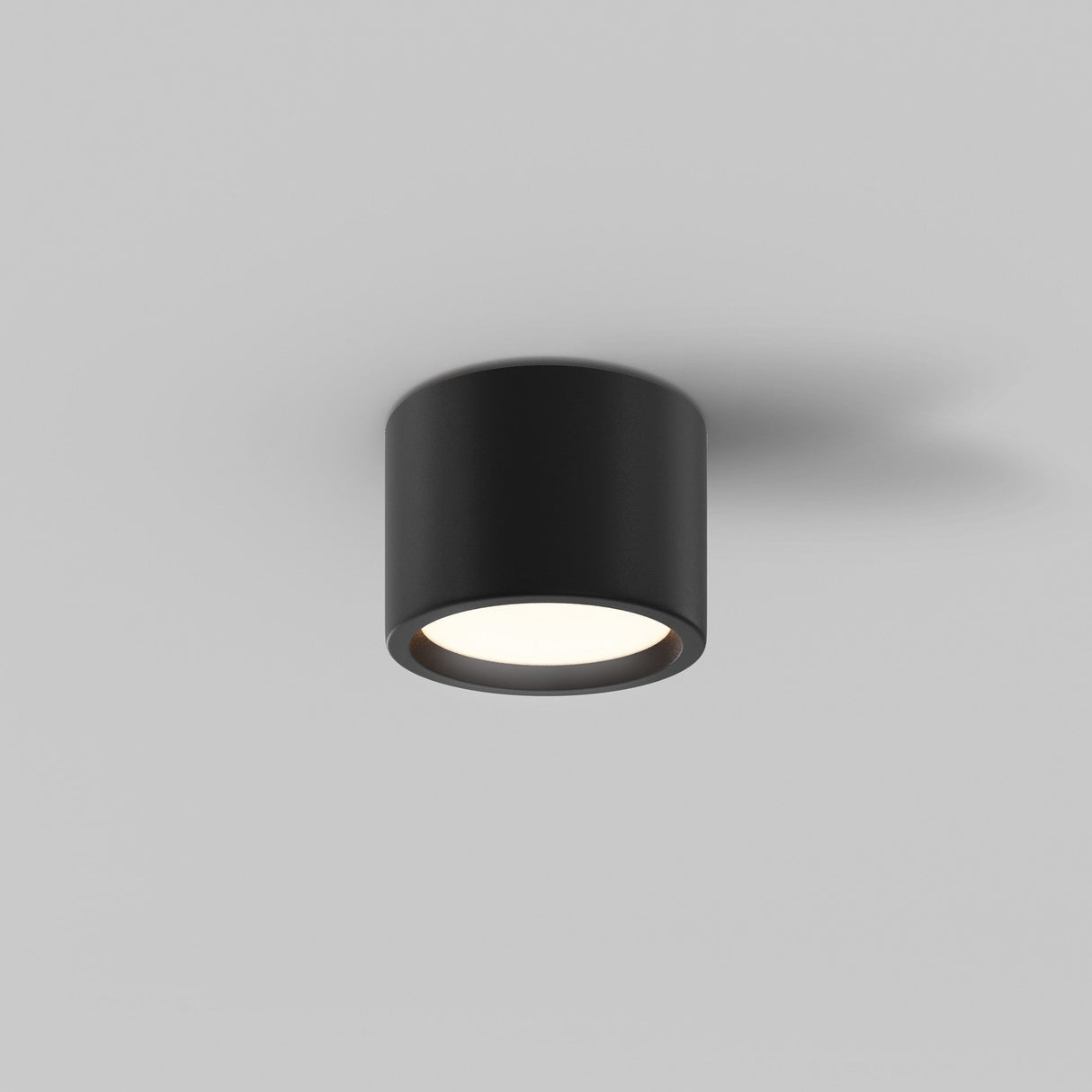 The Hydra LED Round Surface Downlight 10W 3000K in black is mounted on a plain white ceiling, providing energy-efficient illumination with a soft downward glow.