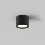 The Hydra LED Round Surface Downlight 10W 3000K in black is mounted on a plain white ceiling, providing energy-efficient illumination with a soft downward glow.
