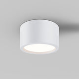 The Hydra LED Round Surface Downlight 15W 3000K in white, IP44 rated, is a modern cylindrical fixture on a light gray ceiling, emitting a soft glow that casts subtle shadows around its edges.