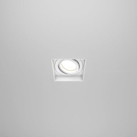 The Atom Single Tilt Square Plaster-in Recessed Downlight - White features a sleek square design and integrates seamlessly into light-colored ceilings, emitting a bright white glow for a minimalist, modern look.