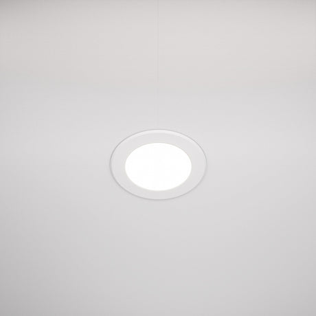 The Stockton CCT LED Round Recessed Downlight 7W 3000-6000K - White is centrally mounted on a neutral white ceiling. It emits a soft glow and thin lines from ceiling panels converge at the fixture, enhancing its energy-efficient design symmetrically.