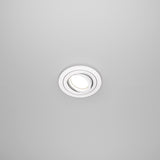 The Atom Single Tilt Round Recessed Downlight - White (DL023-2-01W) features a sleek, modern circular design that provides a minimalist look while illuminating against a plain, light gray ceiling.