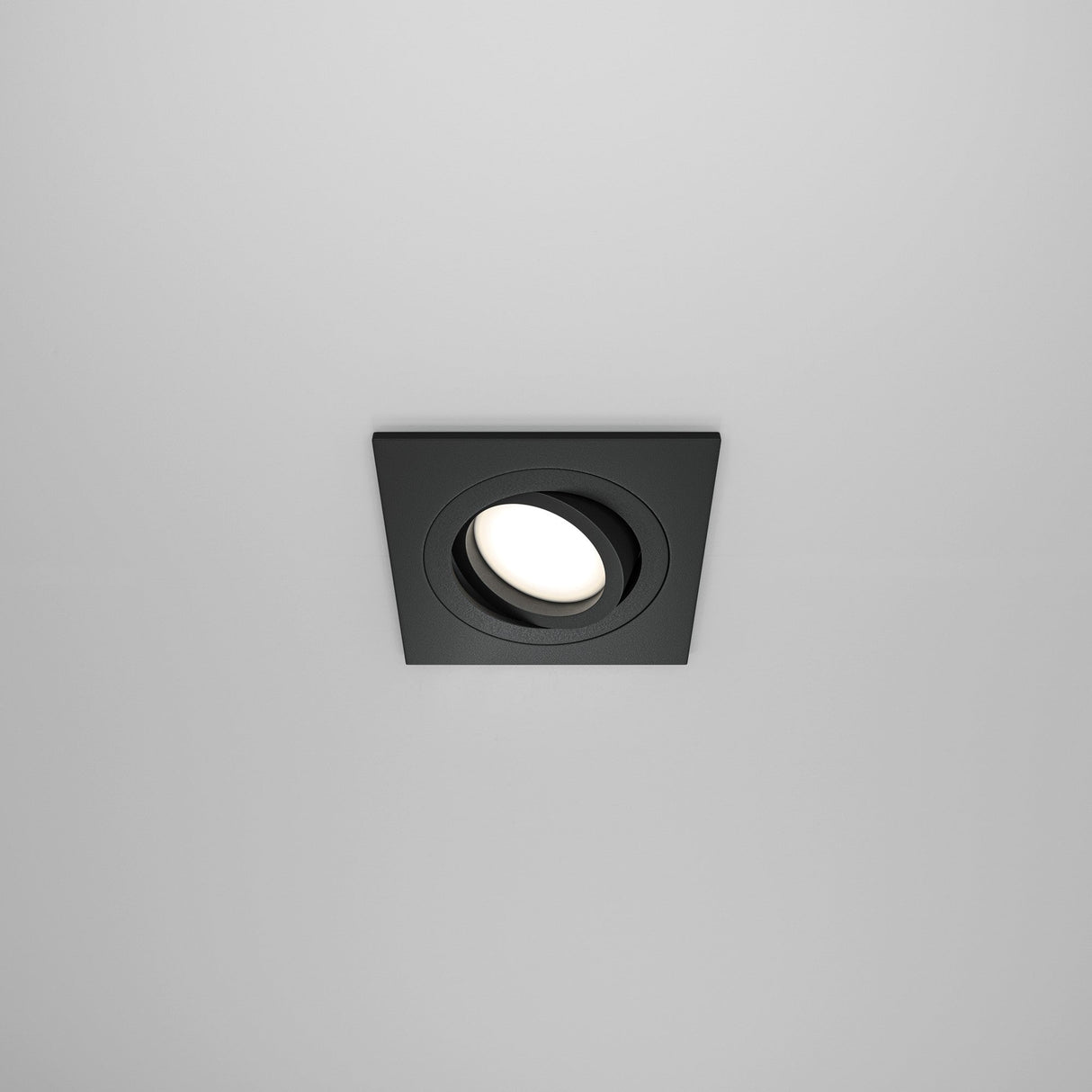 The Atom Single Tilt Square Recessed Downlight in black features a sleek design with a glowing circular center and offers adjustable illumination against a smooth white ceiling.