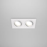The Atom Twin Tilt Recessed Downlight - White is installed in a rectangular fixture against a plain white ceiling. Both adjustable-tilt downlights are illuminated, providing a soft, even glow that enhances the rooms ambient lighting.