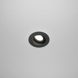 The white ceiling features the Atom Single Tilt Round Recessed Downlight in black, which adds a modern touch. This recessed fixture has an adjustable tilt and emits a soft glow when turned on.