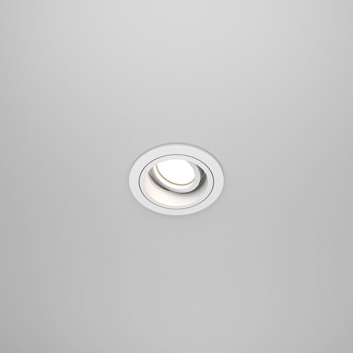 The Atom Single Tilt Round Recessed Downlight - White (DL025-2-01W) is elegantly positioned against a plain white ceiling, featuring an adjustable tilt and modern circular design that highlights contemporary interior design at its finest.