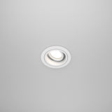 The Atom Single Tilt Round Recessed Downlight - White (DL025-2-01W) is elegantly positioned against a plain white ceiling, featuring an adjustable tilt and modern circular design that highlights contemporary interior design at its finest.