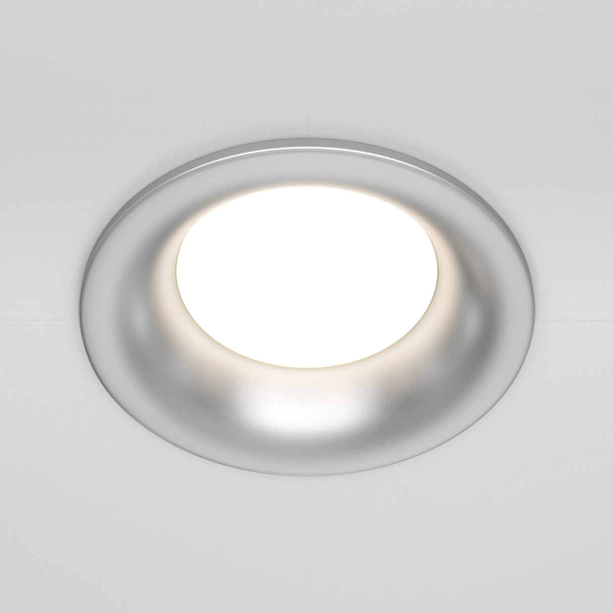 A close-up of the Slim Fixed Round Recessed Downlight - Silver, featuring a circular frame and cast aluminum design, emits a bright glow against the white ceiling.