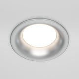 A close-up of the Slim Fixed Round Recessed Downlight - Silver, featuring a circular frame and cast aluminum design, emits a bright glow against the white ceiling.