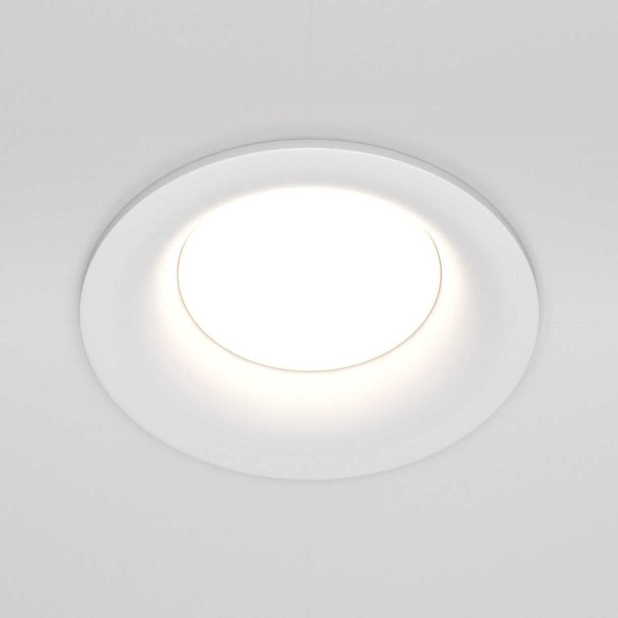 The Slim Fixed Round Recessed Downlight in white is embedded in a plain ceiling, emitting a bright, even glow. Its minimalist design features a smooth trim that blends seamlessly into the ceiling surface.