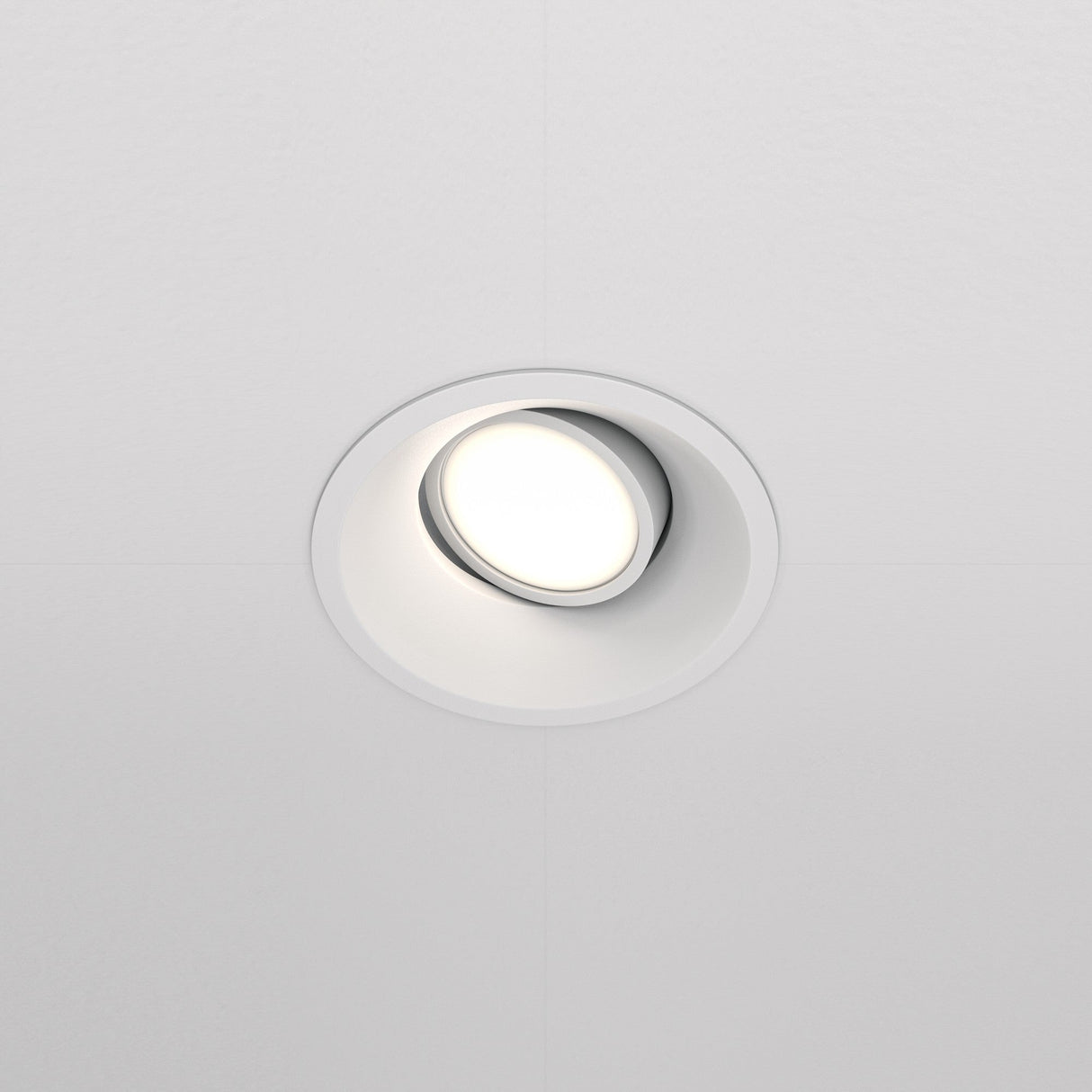The Dot Single Tilt Round Recessed Downlight is installed in a white ceiling, casting a soft white glow. This modern, energy-efficient fixture features an adjustable tilt for versatile lighting.