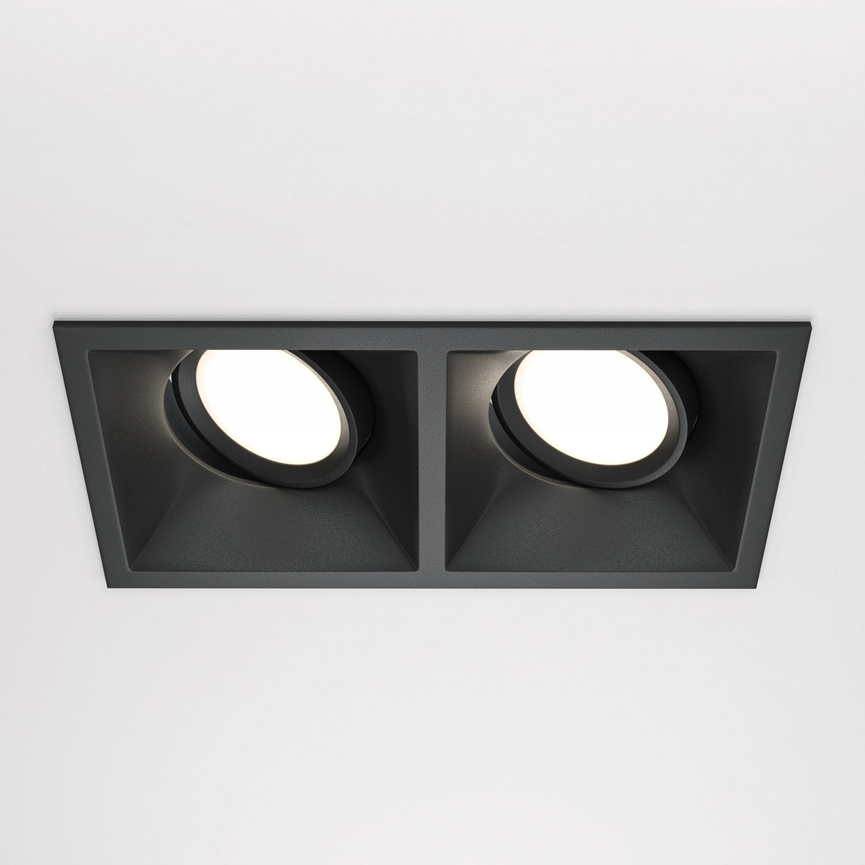 The black Dot Twin Tilt Recessed Downlight, with a minimalist rectangular design, offers bright white energy-efficient LED lighting against a plain white ceiling.