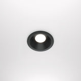The Zoom Single Fixed Round Recessed Downlight - Black features a circular black cast aluminium fixture and a bright white LED bulb, blending seamlessly into a smooth white ceiling. It offers both style and durability with its IP65 rating.