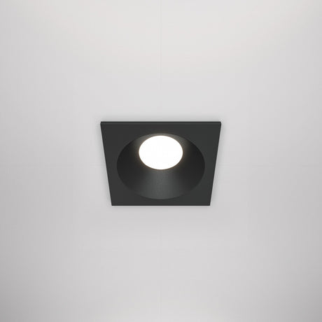 The Zoom Single Fixed Square Recessed Downlight - Black features a central circular bulb, a minimalist black finish for modern appeal, complements any white ceiling, and offers durability with an IP65 protection rating.