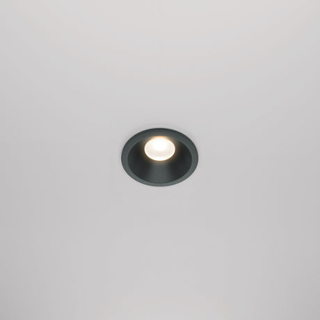 The Zoom LED Dimmable Round Recessed Downlight 6W 3000K in black features a modern, minimalist design. Against a smooth, white ceiling, it emits a soft, bright glow and ensures high color accuracy with its CRI 90 rating.