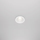 The Zoom LED Round Recessed Downlight 6W 4000K in white is installed in a white ceiling, emitting a soft glow. Its simple, modern design blends seamlessly with the surface, and an IP65 rating ensures durability.