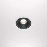 The Zoom LED Round Recessed Downlight 12W 4000K in black casts a bright glow on a white ceiling. Its minimalistic, modern design features an IP65 rating for durability.