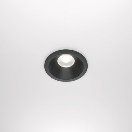 The Zoom LED Round Recessed Downlight 12W 4000K in black casts a bright glow on a white ceiling. Its minimalistic, modern design features an IP65 rating for durability.