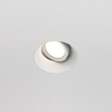 The Dot Single Tilt Plaster-in Round Recessed Downlight in white, embedded in the ceiling, is turned on, emitting a soft, warm glow with its adjustable tilt mechanism providing directional illumination.