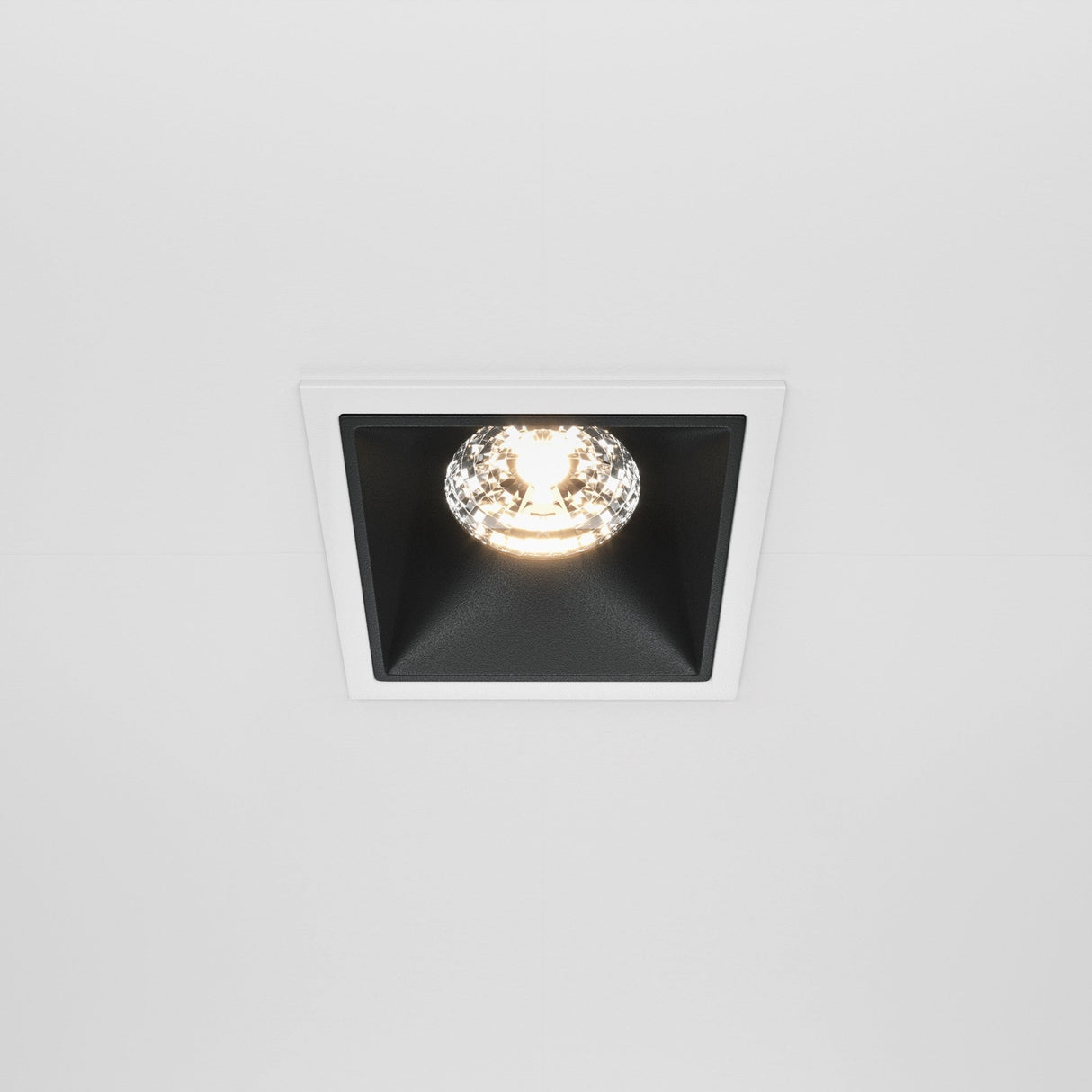 The Alfa LED Dimmable Fixed Square Recessed Downlight 15W 3000K in white and black is turned on, featuring a two-tone design with a centered bulb against a black interior, creating striking contrast and enhancing modern interior lighting.
