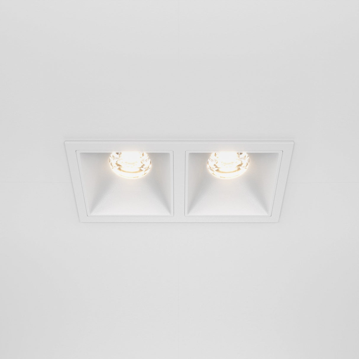 A sleek white ceiling features the Alfa LED Dimmable Fixed Square Recessed Twin Downlight, 20W, 3000K. Each fixture has a circular bulb emitting warm white light, showcasing clean lines and symmetry in a modern, minimalist design.